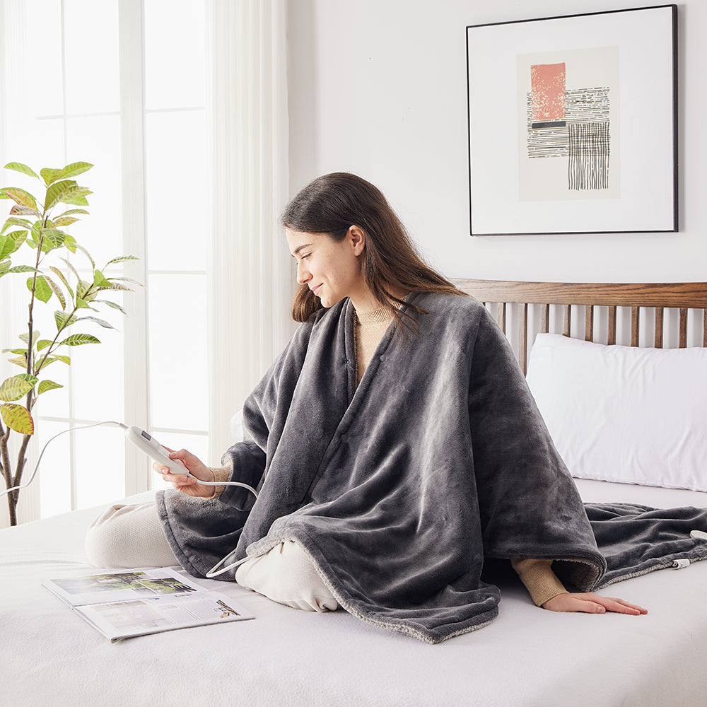 Une femme assise sur le lit dans le poncho chauffant règle la chaleur avec la commande