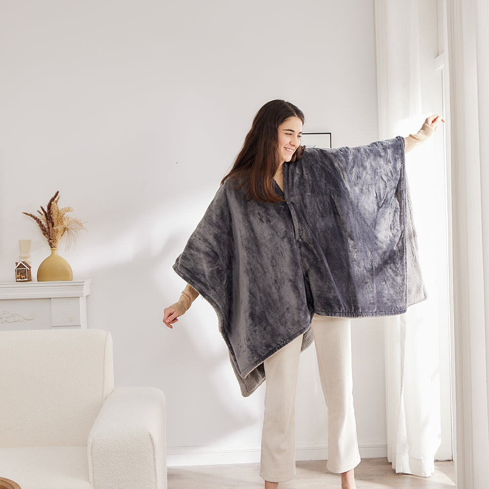 Une femme debout dans le salon porte le poncho chauffant gris, les bras écartés