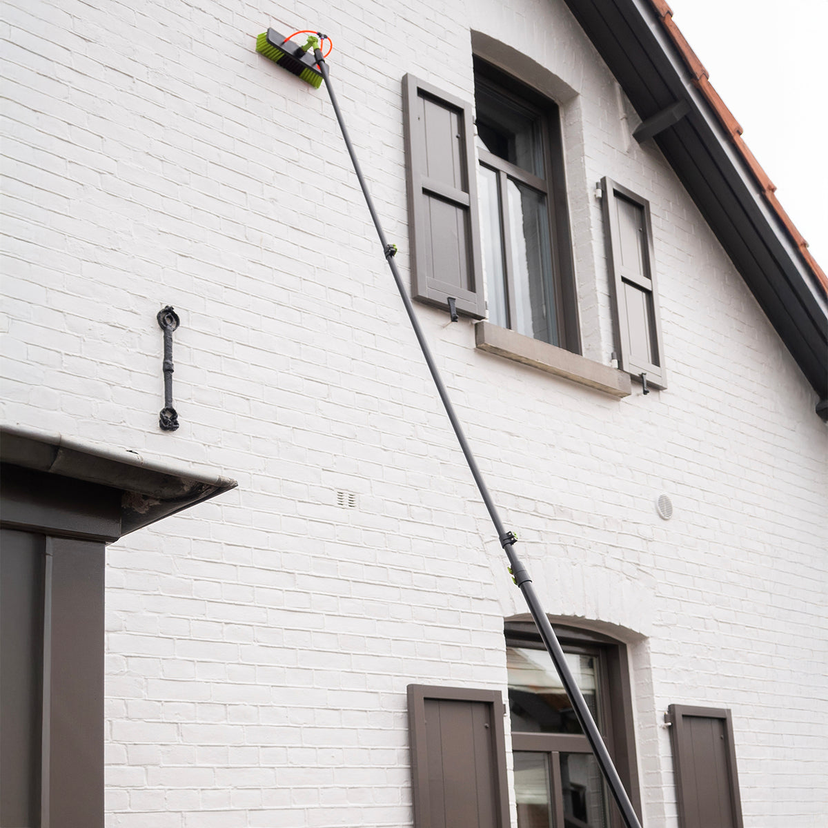 La brosse de lavage déployée nettoie la façade d'une maison blanche jusqu'à la gouttière