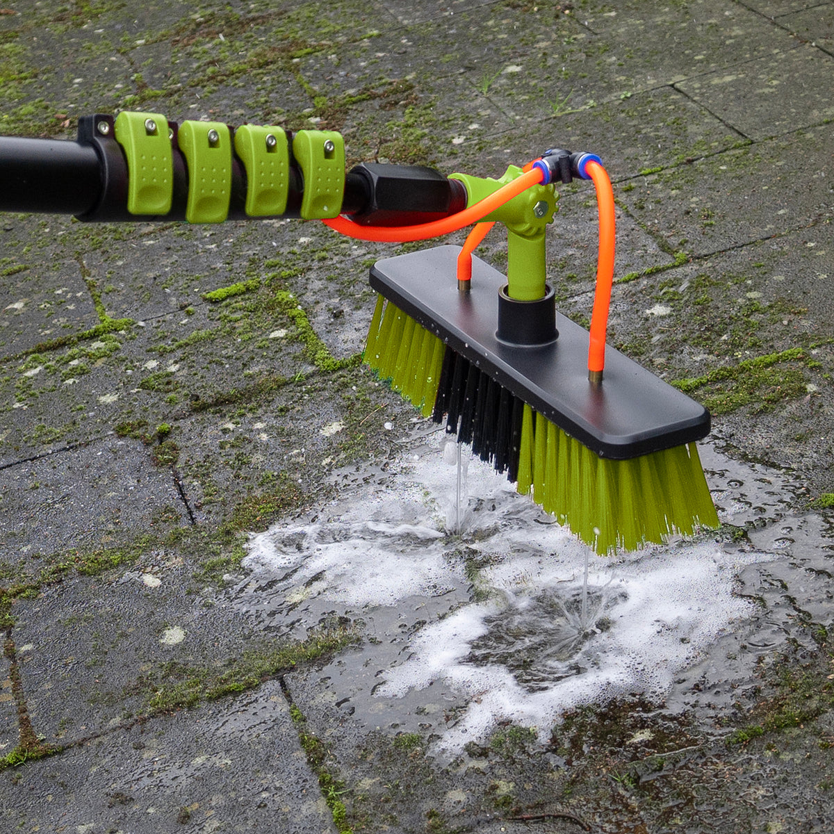 La brosse de lavage décrasse des dalles de terrasse verdies avec de la mousse de savon