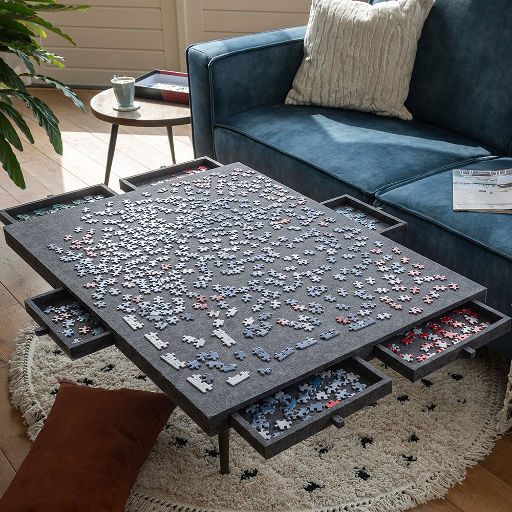Grand plateau de puzzle en feutre sur une table basse, tiroirs ouverts remplis de pièces