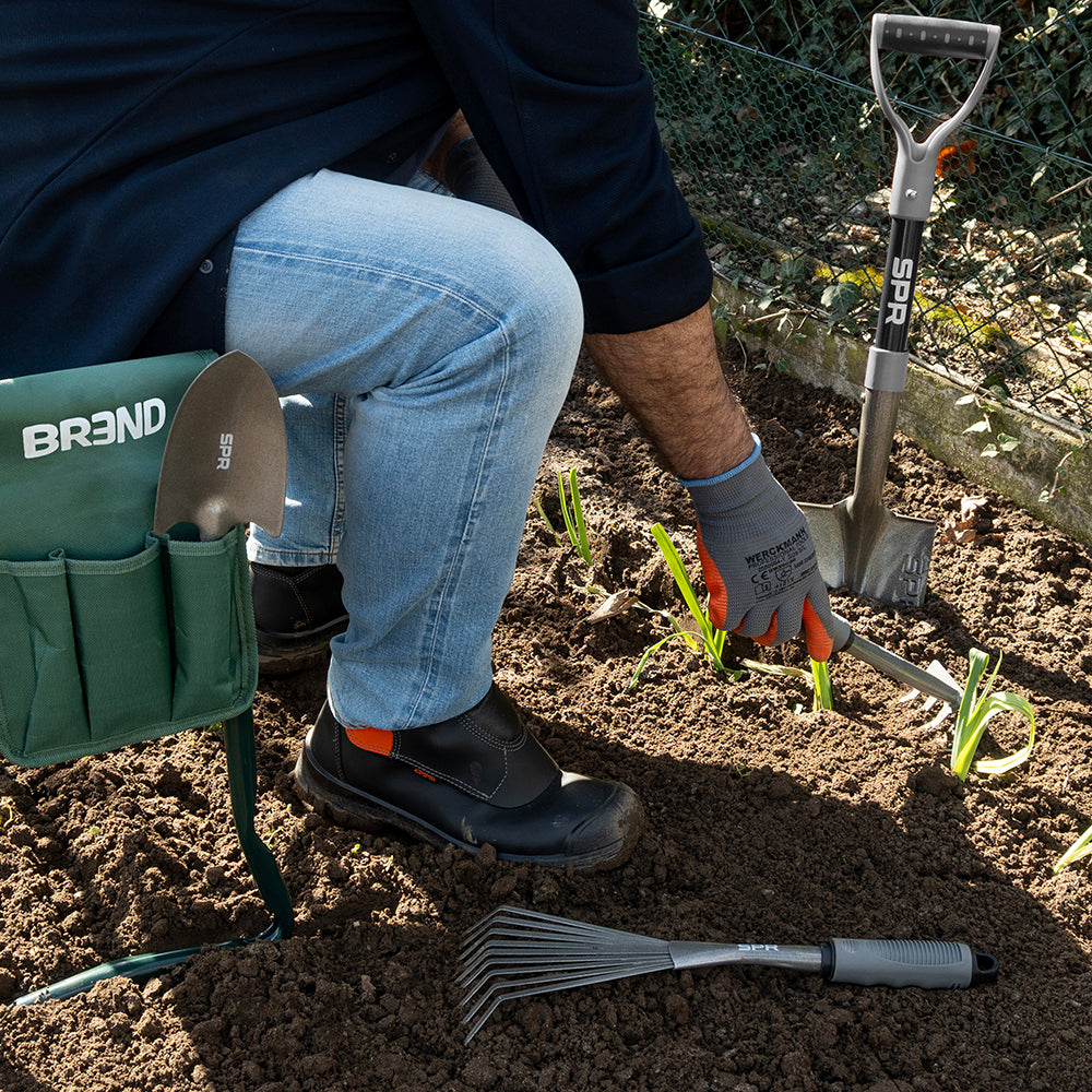 Man op de tuinkruk werkt in de moestuin, met de mini-bladhark en de spade naast zich