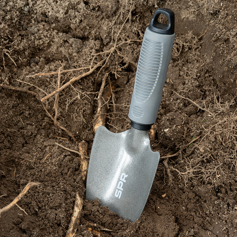 Brede schep staat in de aarde tussen boomwortels