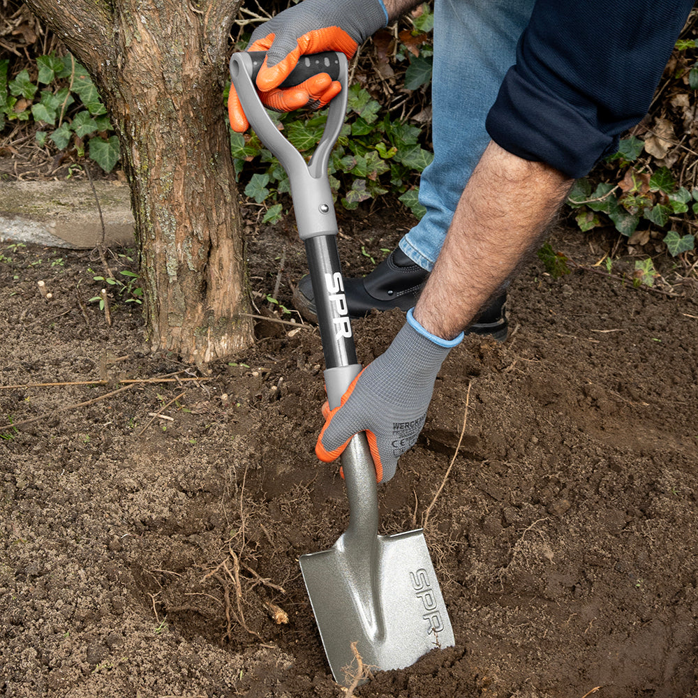 Man steekt de spade met getande rand in de grond bij een boom